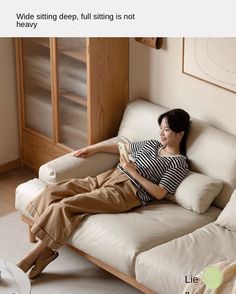 a woman sitting on top of a white couch next to a wooden cabinet and window