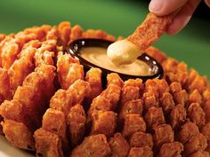 a person dipping some kind of sauce on top of fried food with tater tots