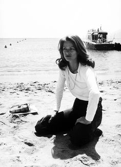 a woman sitting on the beach next to a body of water