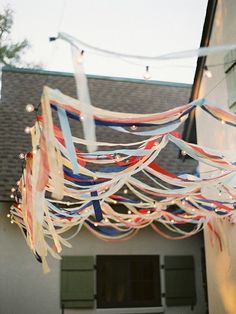 an outdoor party with streamers, lights and decorations hanging from the ceiling in front of a house