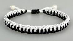 white and black braided bracelet with pearl beads on grey background, closeup view