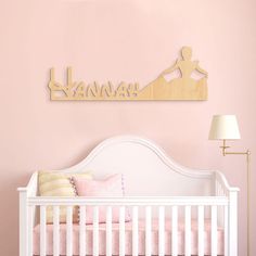 a white crib in a pink room with a wooden name sign above the crib