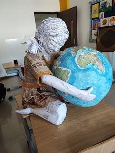 a paper mache man sitting on top of a wooden table next to a globe