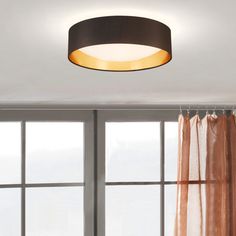 a round light fixture hanging from the ceiling in front of a window with sheer curtains