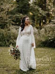 a woman in a white dress holding a bouquet and standing in the grass with trees behind her