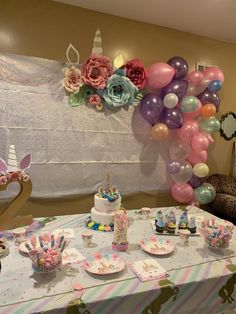 a table topped with lots of cake next to a wall covered in balloons and flowers