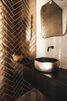 a bathroom with a black sink and gold tile on the wall, along with a large mirror