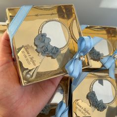 a person holding up three small gold boxes with blue ribbons and flowers on the sides