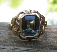 This is a really pretty antique ring. There are two little worn marks on the inside, it has been tested and is 14K gold. I brought the ring to my jeweler, and he looked at the stone under refractive light and identified it as synthetic spinel. Really pretty shade of green. This ring weighs 5.5 grams. The mount is really compelling with each side having a three petal ring in the mount. The face of the ring measures 3/4" across and 5/8" from top to bottom. This ring rests at a size 7.5 on a mandrel. Lovely! Victorian 14k Gold Topaz Ring For Formal Occasions, Formal Victorian 14k Gold Topaz Ring, Antique 14k Gold Hallmarked Topaz Ring, Antique Yellow Gold Topaz Ring Collectible, Antique Yellow Gold Topaz Ring, Vintage Gemstone Engraved Ring Collectible, Vintage Topaz Ring With Intricate Design For Formal Occasions, Vintage Engraved Gemstone Ring For Collectors, Vintage Engraved Topaz Ring Gift