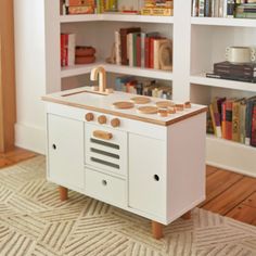 a play kitchen with bookshelves in the background and a rug on the floor