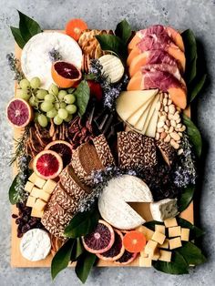 an assortment of cheeses and meats on a wooden platter with green leaves