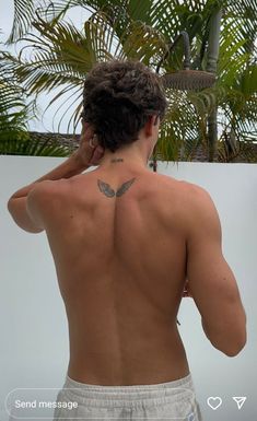 a man with a butterfly tattoo on his back is standing in front of a palm tree