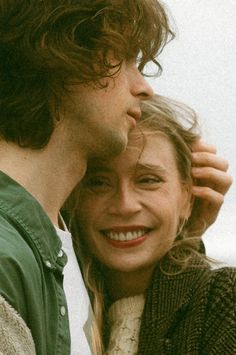 a man and woman standing next to each other with their arms around one another smiling