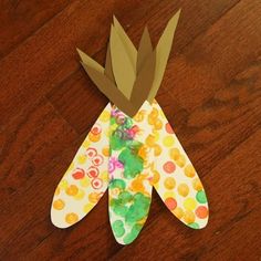 a paper flower with leaves on it sitting on top of a wooden table next to a pair of scissors