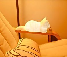 a white cat sitting on top of a wooden chair next to a pillow and lamp