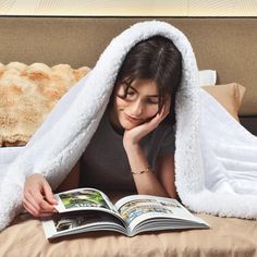 a woman laying in bed under a blanket reading a book