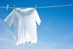 a white t - shirt hanging on a clothesline against a blue sky with clouds