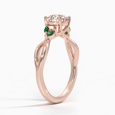 a rose gold ring with green and white stones on the sides, in front of a white background