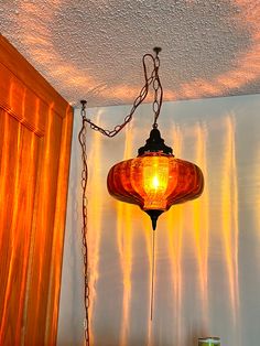 a lamp hanging from the ceiling in front of a wallpapered room with orange curtains