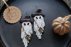 two white and black beaded earrings sitting on top of a plate next to a pumpkin