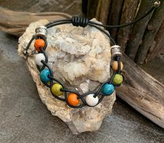 a bracelet with multi colored beads on top of a rock next to a piece of driftwood