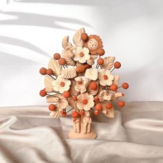 a wooden sculpture of flowers and leaves on a white cloth covered table with a shadow cast in the background