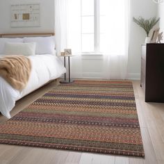 a bed sitting next to a window on top of a wooden floor in a bedroom