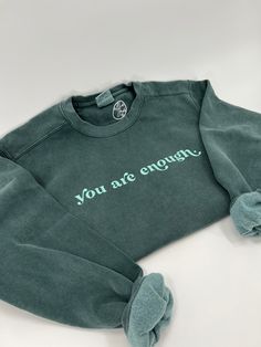 a green sweatshirt with the words you are enough written on it and two slippers laying next to it