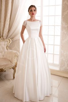 a woman in a white wedding dress standing next to a chair and window with curtains