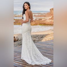 a woman in a wedding dress standing on a wooden deck near the ocean with her back to the camera