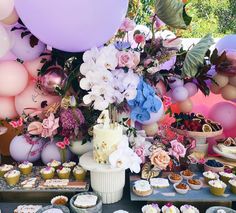 a table topped with lots of cupcakes and cake next to balloons in the air