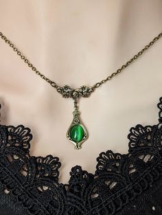 Welcome to our vintage-inspired world where elegance meets history! Dive into the allure of yesteryears with our Emerald Green Pendant Necklace, a timeless piece reminiscent of Victorian charm and historical costume jewelry. Crafted with meticulous attention to detail, this necklace features a captivating emerald green cats eye cabochon set in an elegant teardrop shaped antiqued brass pendant. Each pendant whispers tales of romance and elegance, capturing the essence of Victorian aesthetics. Emb Cheap Elegant Green Necklaces, Cheap Symbolic Green Jewelry, Medieval Jewelry Emerald, Cheap Green Vintage Necklace, Cheap Green Retro Necklace, Cheap Retro Green Necklace, Emerald Green Vintage Necklace, Luxury Green Victorian Necklaces, Shoulder Necklace Emerald