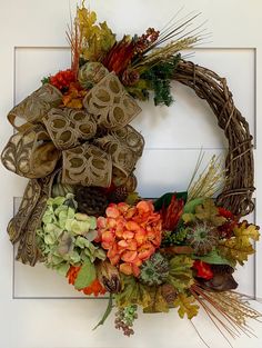 a wreath is hanging on the door with autumn flowers and leaves in front of it