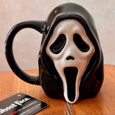 a black and white coffee mug with a ghost face on it's side next to a credit card