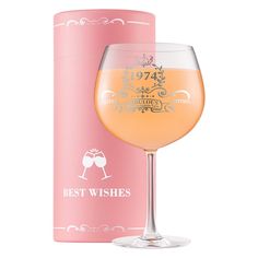 a glass of wine next to a pink box on a white background with the words best wishes written in gold