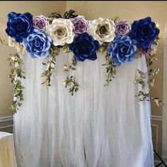 a white curtain with blue and purple flowers hanging from it's sides in front of a wall