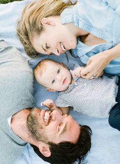 a man and woman laying on the ground with their baby in his lap, smiling at the camera