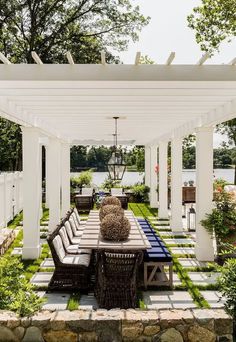 an outdoor dining area with white pergoline and wooden table, chairs and benches