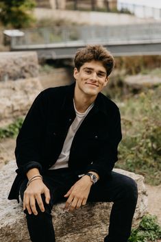 a young man sitting on top of a rock