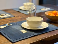 a bowl of oranges sits on a placemat next to a cup and saucer