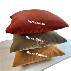 three pillows that say terracotta, olive green, rust yellow and olive green