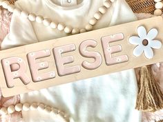 a wooden sign that says reese on it next to some pearls and beads with a flower