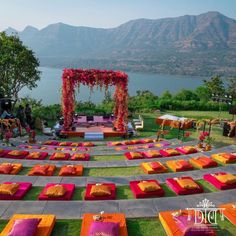 an outdoor ceremony set up with orange and pink linens on the grass near water