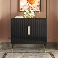 a black cabinet with gold handles and flowers on top in front of a pink wall