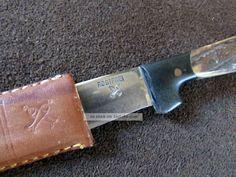 a knife that is laying on the ground next to a leather sheath with writing on it