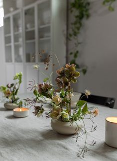 three vases filled with flowers on top of a table next to two lit candles