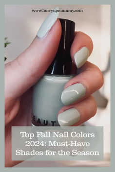 Close-up of a hand holding a nail polish bottle with glossy, muted sage green nails, a popular Autumn Nails color for 2024. Nail Colors For Pale Skin Fall, Nail Colors 2024 Fall, Fall 2024 Nail Colors, Neutral Fall Nail Colors, Nail Colors For Pale Skin