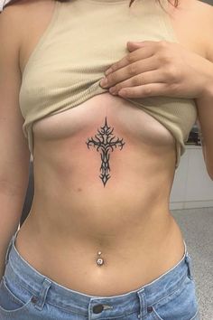 a woman with a cross tattoo on her stomach is looking at the camera while holding her hand up to her chest