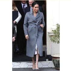 a woman in a gray coat is walking out of a door with other people behind her