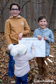 three children standing in the leaves holding up a poster